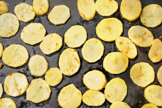 Potatoes sliced to thin circles, seasoned with spices, grilled on electric grill, view from above