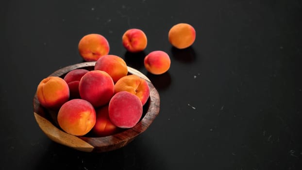 Apricots in small wooden bowl, some spilled on black table, space for text right side