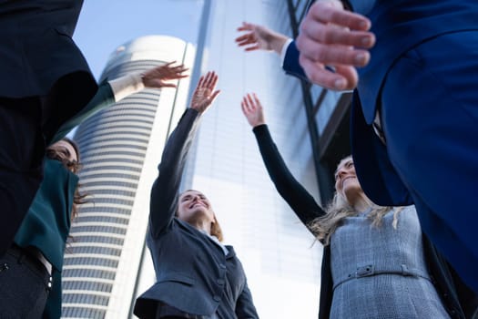Young team of business executives raising arms while standing outdoors in an office area.