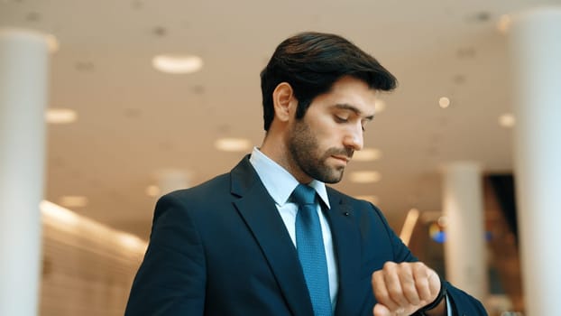 Caucasian smart business man looking at watch while waiting colleague. Executive manager wearing suit while standing at mall with blurred background. Investor wear blue suit check time. Exultant.