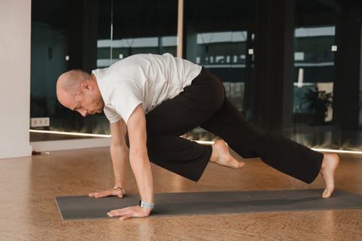 An athletic young man does exercises in the fitness room. A professional guy does yoga in the gym.