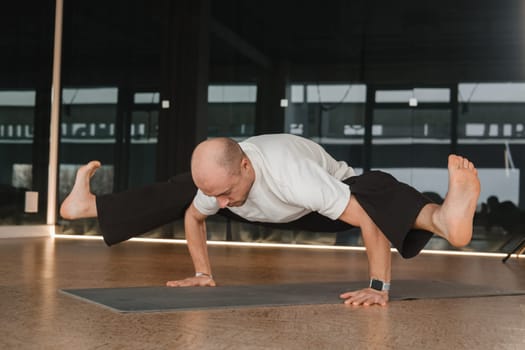 An athletic young man does exercises in the fitness room. A professional guy does yoga in the gym.