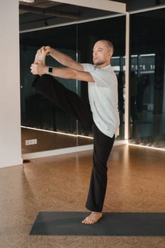 An athletic young man does exercises in the fitness room. A professional guy does yoga in the gym.