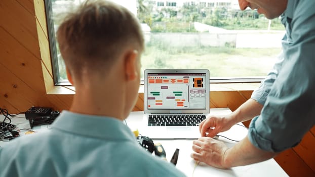 Closeup of caucasian teacher hand picking wires and teaching about electronic equipment while boy looking at instructor using electric tool at table with laptop display coding screen. Edification.