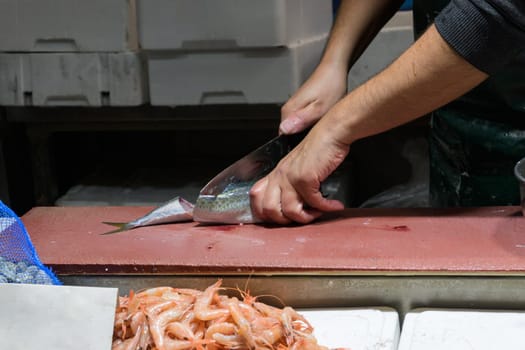 Closeup of male worker's hands cutting fish with knife at table.