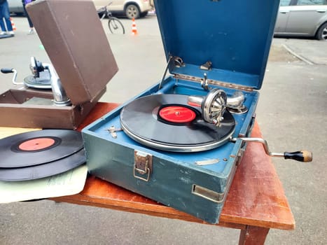 An old retro record playing on old vintage gramophone at flea market. Work of portable gramophone. Old vintage shabby record player, phonograph, potefone. Needle. Nostalgia antique audio turntable