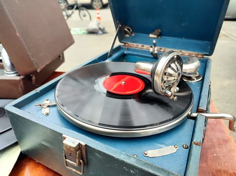 An old retro record playing on old vintage gramophone at flea market. Work of portable gramophone. Old vintage shabby record player, phonograph, potefone. Needle. Nostalgia antique audio turntable