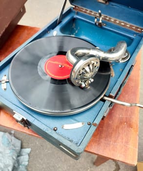 An old retro record playing on old vintage gramophone at flea market. Work of portable gramophone. Old vintage shabby record player, phonograph, potefone. Needle. Nostalgia antique audio turntable