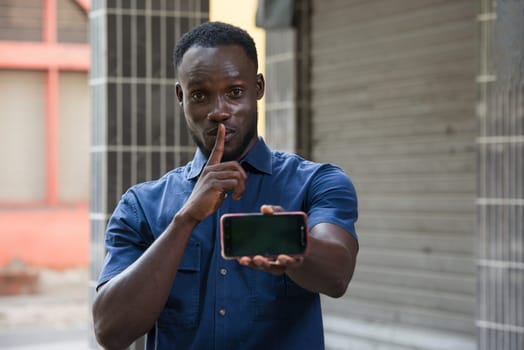 excited man expressing surprise on face and showing phone screen and having silence gesture with finger on mouth