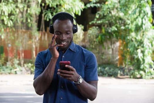 young man standing outdoors looking at mobile phone while smiling.