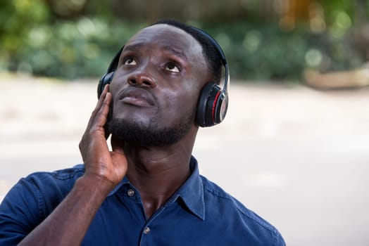 Young man standing outdoors listening to music using headphones while looking up.