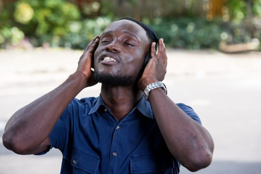 Young man standing outdoors listening to music using headphones while smiling.