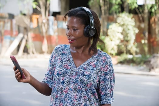 young woman standing outdoors looking at cell phone while smiling.