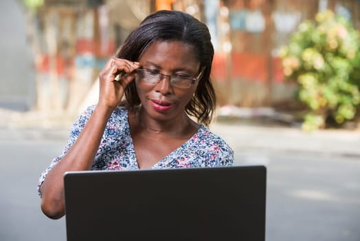 young woman sitting outside in glass looking at laptop smiling.