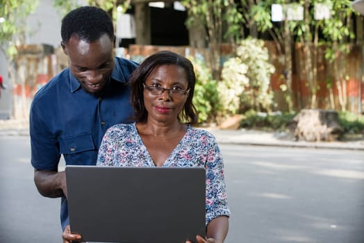 young woman sitting with laptop watching the camera while smiling while her boyfriend looks at laptop.