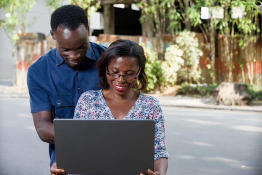 young couple outdoors looking at laptop smiling.