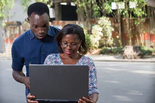 young couple outdoors looking at laptop smiling.