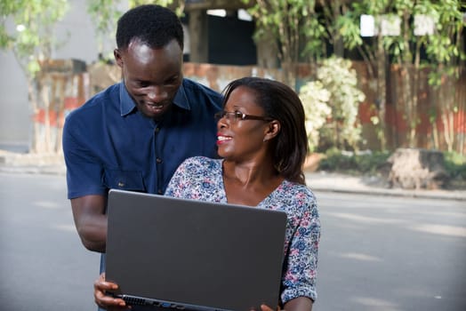 young woman sitting with laptop watching her boyfriend while he looks at the laptop smiling.