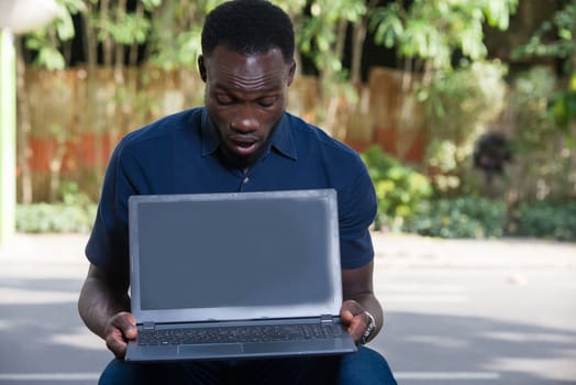young man sitting outdoors looking at laptop with surprise.