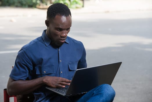 young man sitting outdoors looking at laptop with discontent.