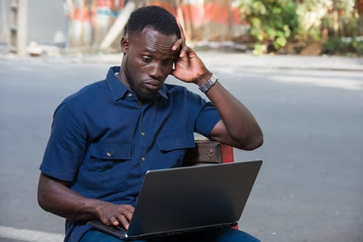 young man sitting outdoors with laptop thinking.