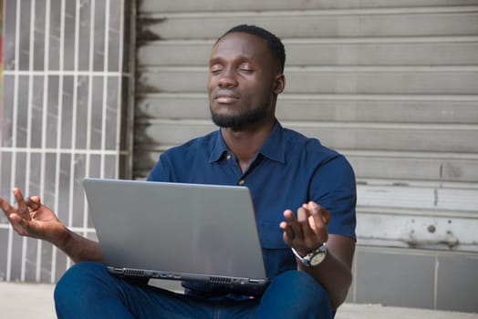 young man sitting on the floor with laptop thinking with eyes closed.