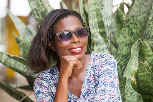 young woman sitting in a park looking at the camera hand under the chin smiling.