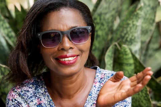 young woman sitting in a park in sunglasses watching the camera smiling.