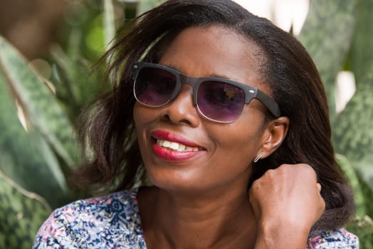 young woman sitting in a park in sunglasses watching the camera smiling.