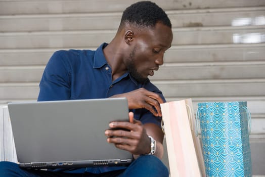 young man sitting on the floor with laptop watching in shopping bag.