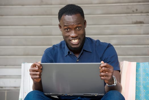 young man sitting on the floor with shopping bags and laptop looking at camera laughing.