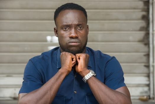 young man in blue shirt sitting outdoors thinking of fists under chin.