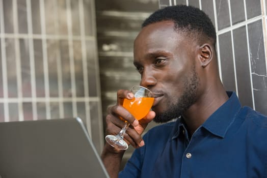 young man in blue shirt sitting near a wall go drinking fruit juice smiling.