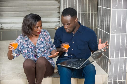 young couple sitting on the floor talking to each other smiling with glasses of juice in hand.