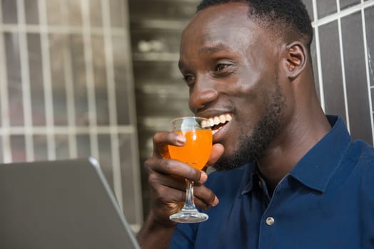 young man in blue shirt sitting near a wall smiling smile with a glass of juice near the mouth.