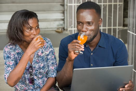 young couple sitting outside with laptop drinking fruit juice smiling.