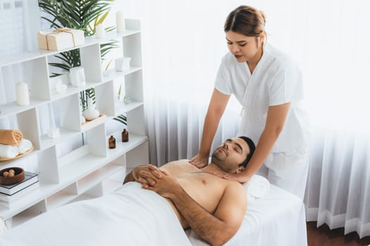 Caucasian man customer enjoying relaxing anti-stress spa massage and pampering with beauty skin recreation leisure in day light ambient salon spa at luxury resort or hotel. Quiescent