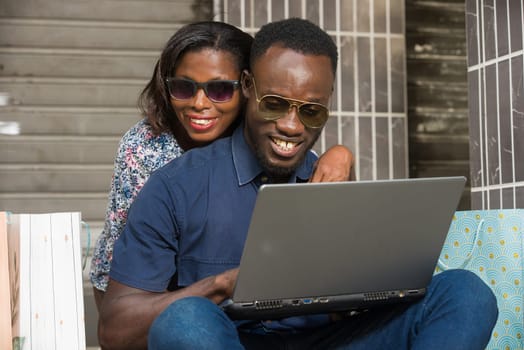 Happy couple using a laptop sitting outside and spending time together after doing a shopping