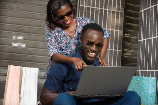 Happy couple using a laptop sitting outside and spending time together after doing a shopping