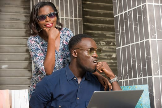 young couple sitting with shopping bags and using a laptop to make online purchases. couple in sunglasses looking at each side