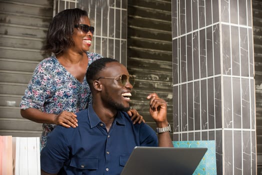 young couple sitting with shopping bags and using a laptop to make online purchases. couple laughing and looking sideways