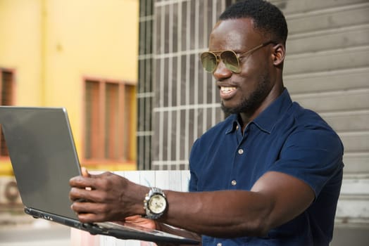 young man sitting outside looking at laptop smiling.