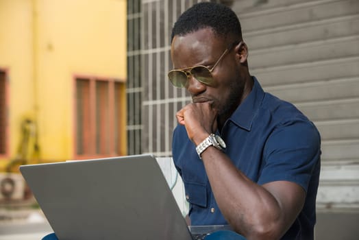 young man sitting outside thinking about looking at laptop.