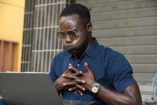 young man sitting outside thinking about looking at laptop.