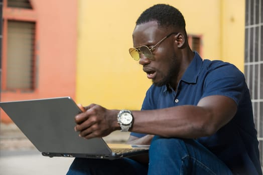 young man sitting outside looking at laptop with surprise