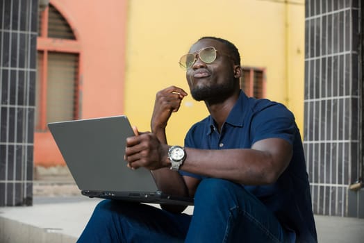 young man sitting outside looking up with laptop in hand.