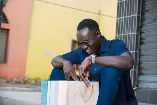 young man sitting outdoors looking in shopping bag smiling.
