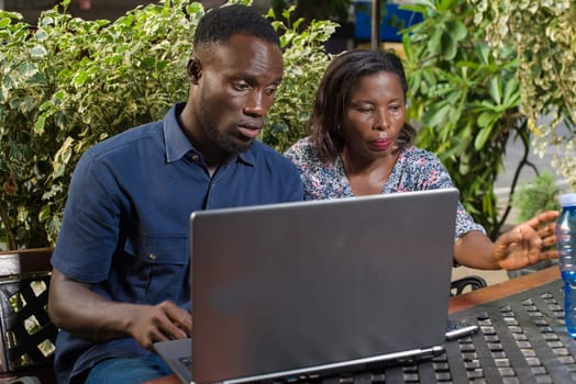 young couple sitting in a park watching laptop.