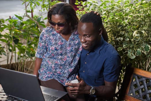 young couple sitting in a park looking at laptop smiling.