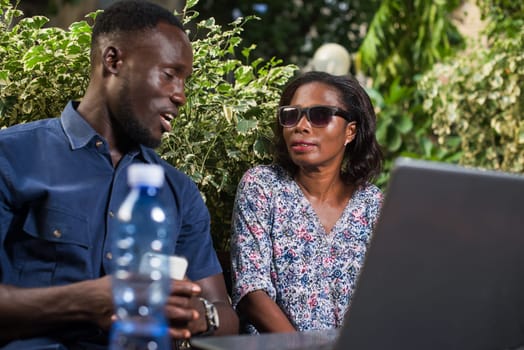 young couple sitting in a park with laptop talking.